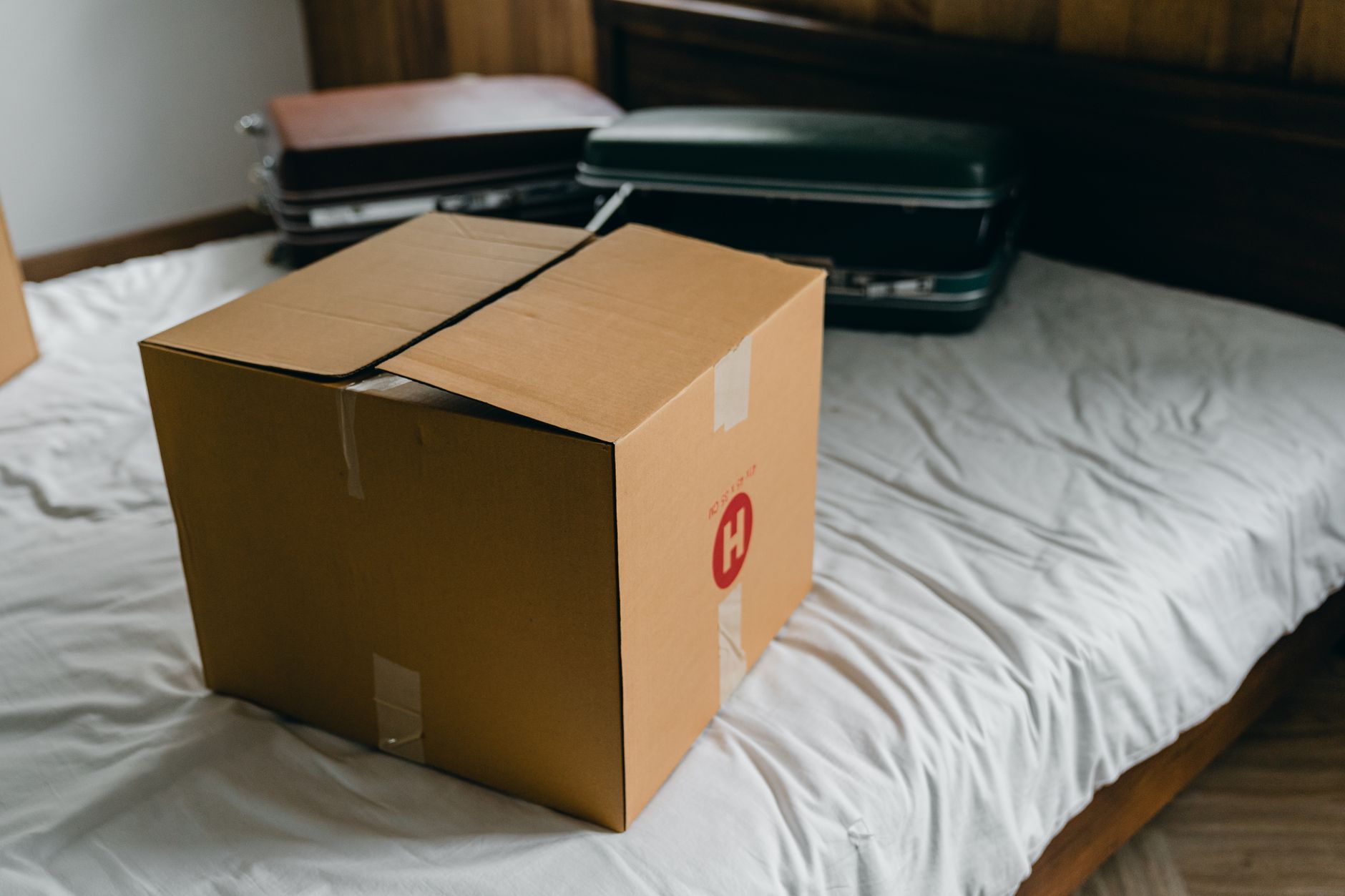From above of cardboard package placed on bed near suitcases before unpacking belongings after moving in new home — Discover