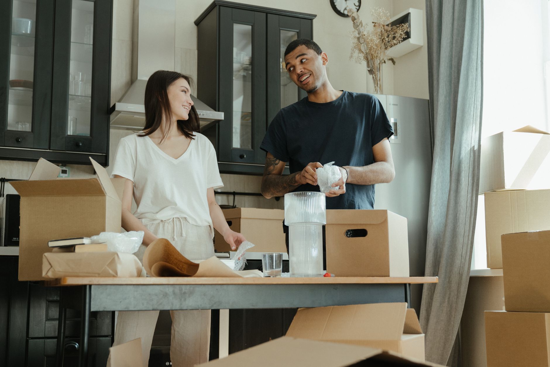 Smiling couple unpacking boxes in their new home kitchen, ready for a fresh start. — Packing Tips For Motorcycle Trips