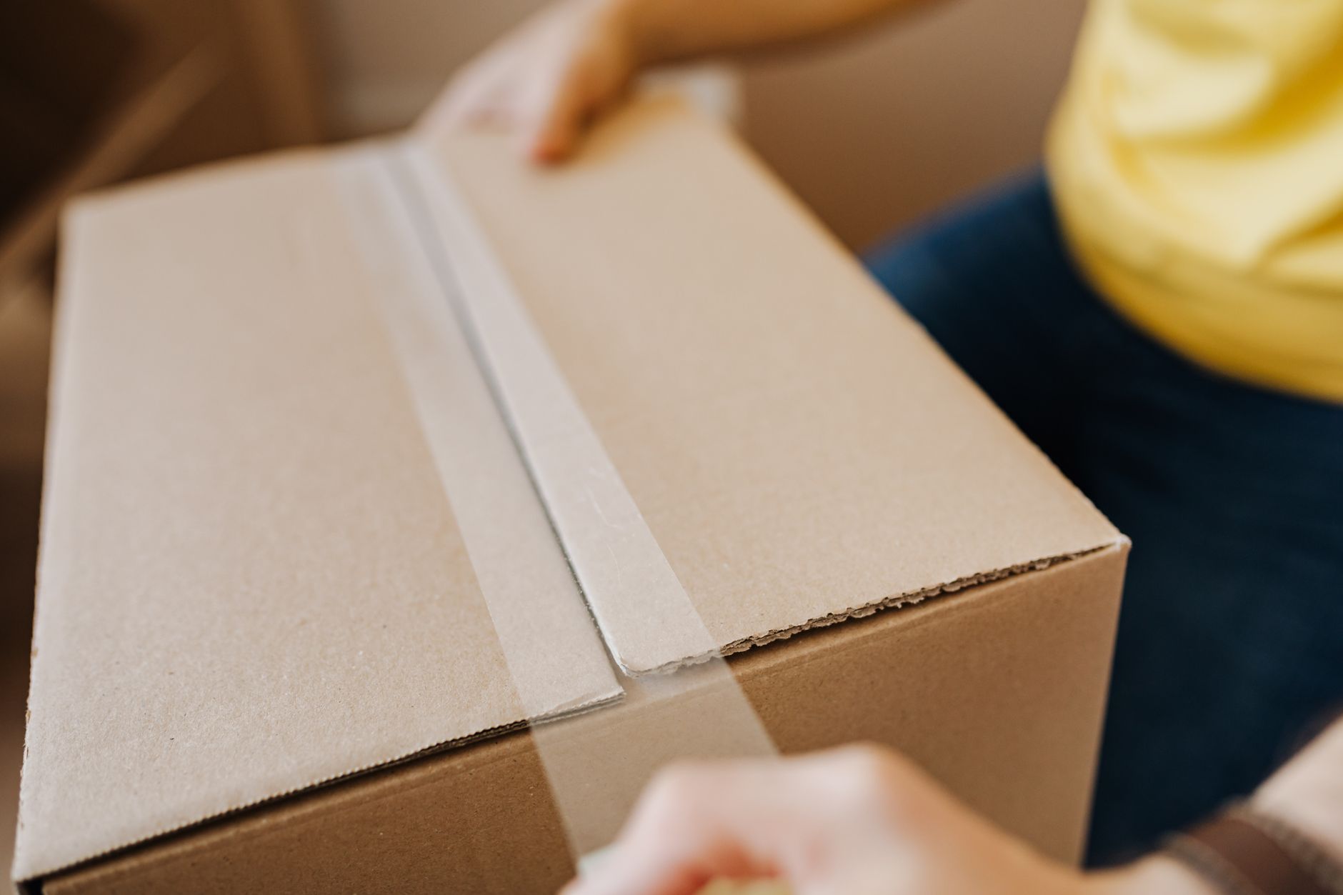 Crop anonymous courier in yellow shirt packing purchase and sealing carton box with tape before deliver — Rules Followed By P